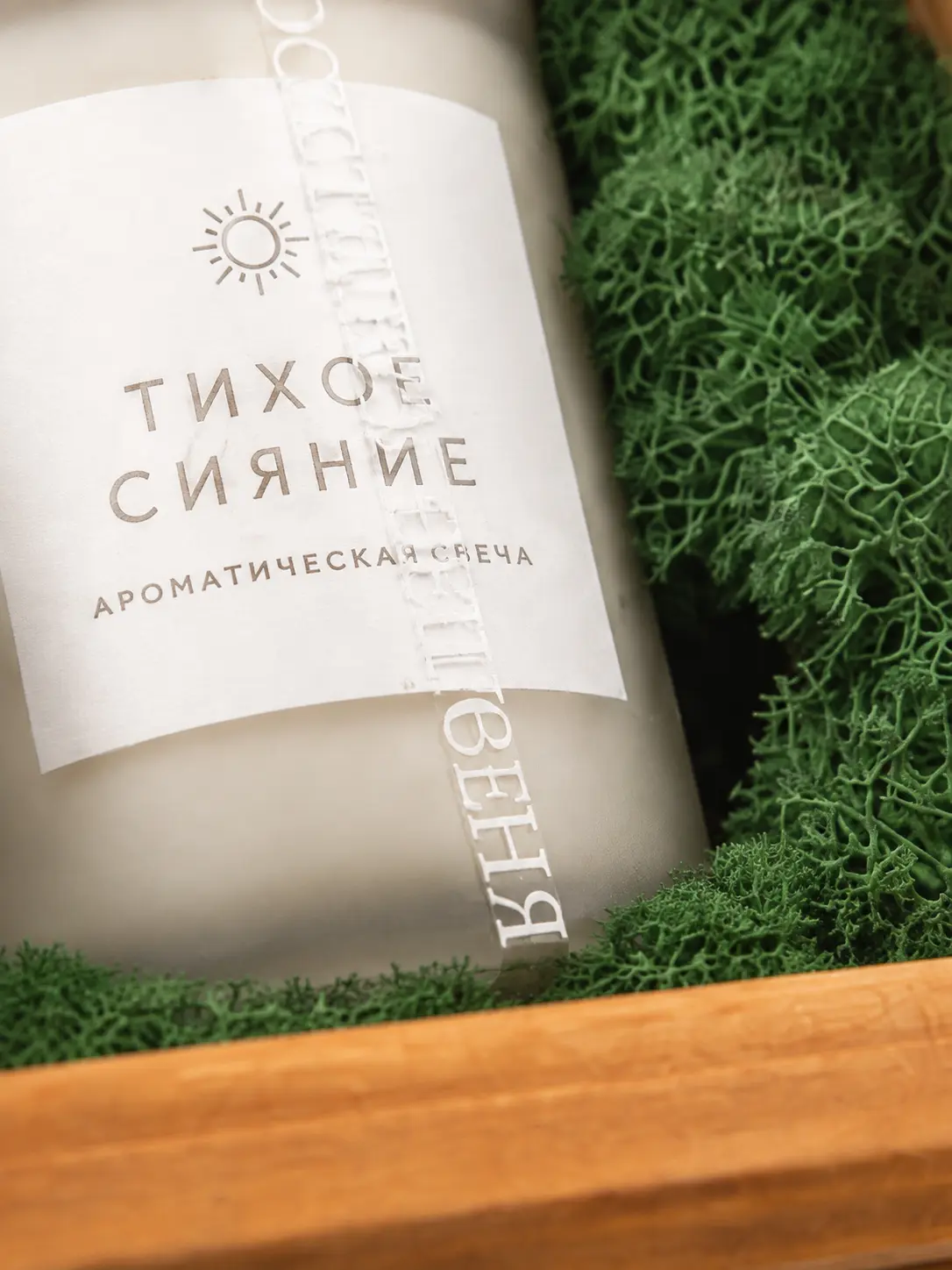 Крупный план ароматической свечи «Тихое сияние» среди зелёного декора в деревянной коробке